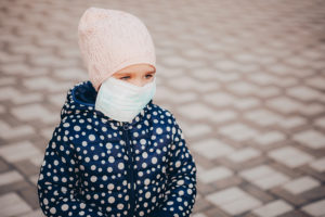 Little girl in protection mask outdoors. child plays in the street